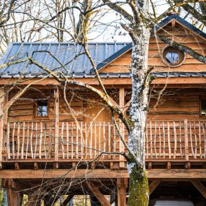 Cabane perchée en bois, nichée entre les arbres, avec un balcon accueillant.
