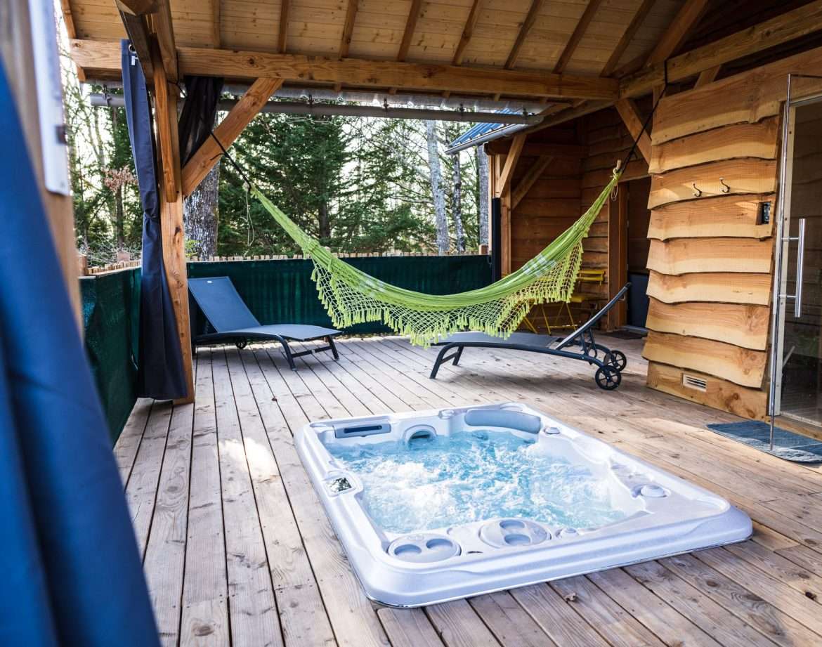 Cabane en bois avec jacuzzi et hamac sur une terrasse en bois. Détente assurée !