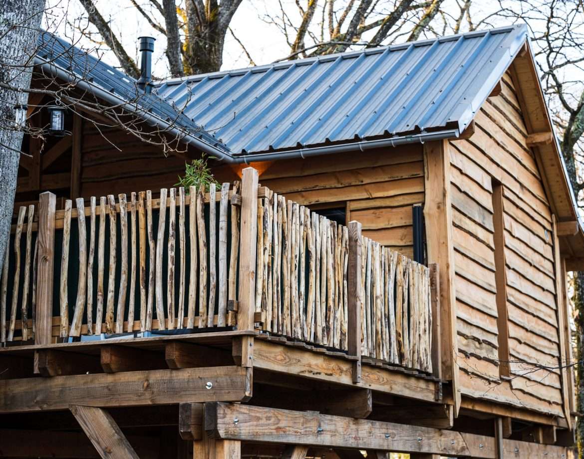 Cabane perchée en bois avec balcon en rondins, nichée dans les arbres.