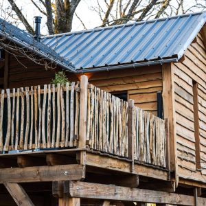 Cabane perchée en bois avec balcon en rondins, nichée dans les arbres.