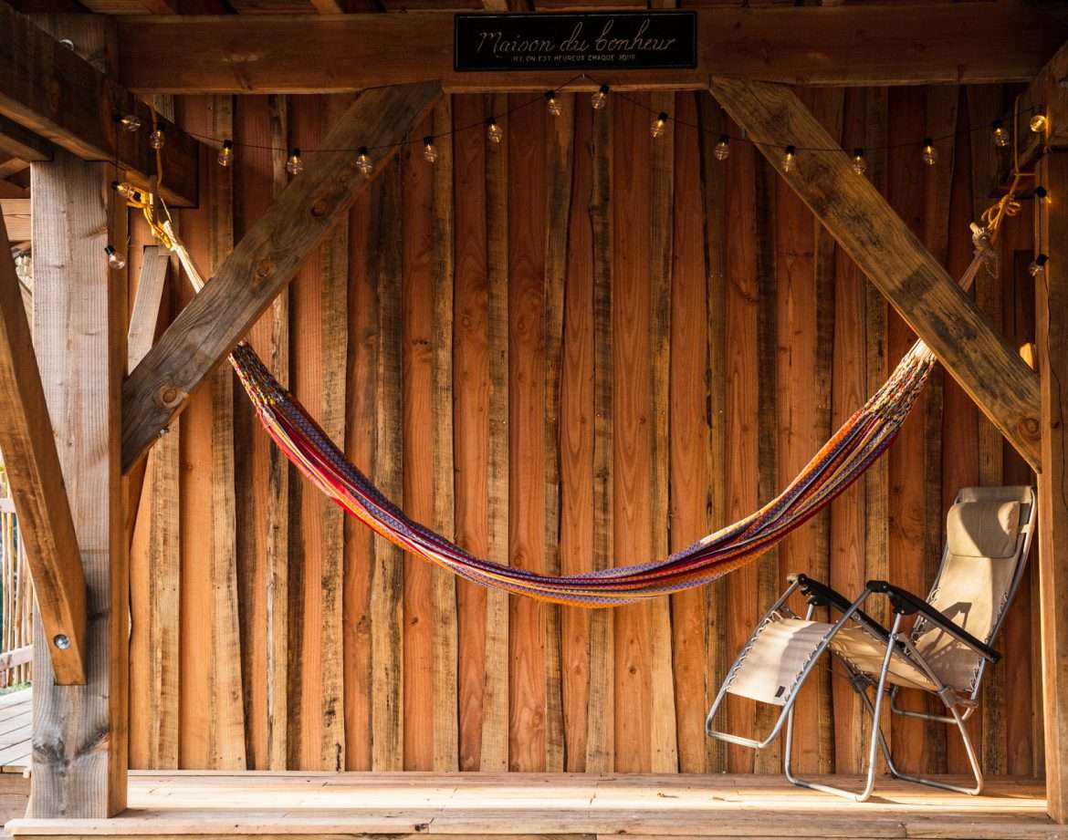 Hébergement insolite : une cabane en bois avec un hamac coloré et des chaises confortables.