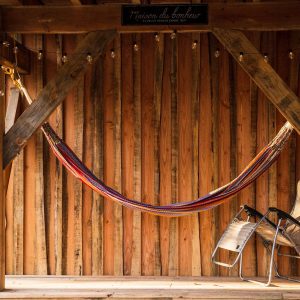 Hébergement insolite : une cabane en bois avec un hamac coloré et des chaises confortables.