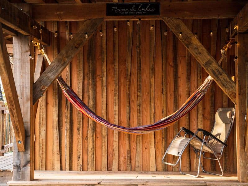 Hébergement en bois avec hamac coloré et chaise pliante sur une terrasse chaleureuse.