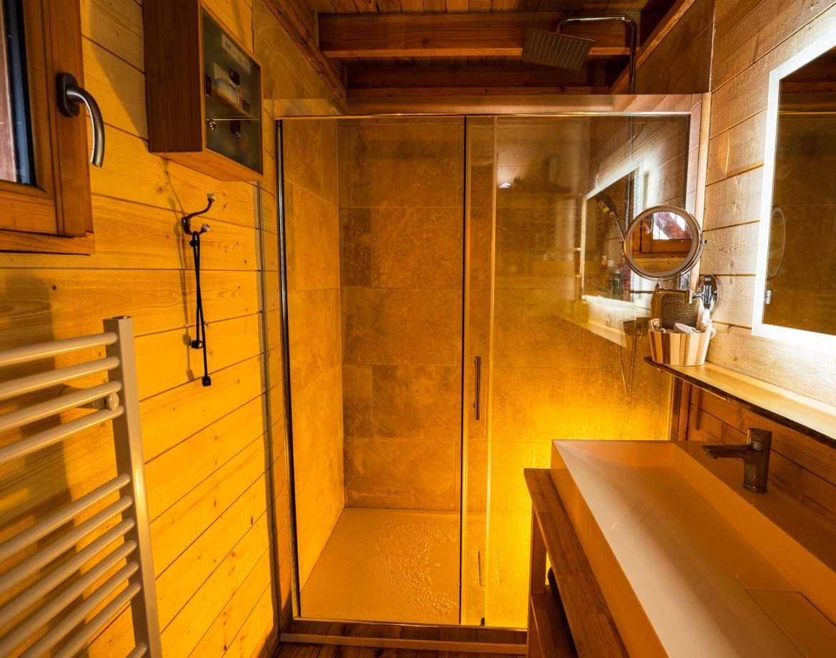 Salle de bain en bois dun chalet insolite, avec douche vitrée et éclairage chaleureux.