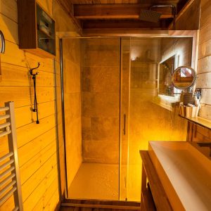 Salle de bain en bois dun chalet insolite, avec douche vitrée et éclairage chaleureux.