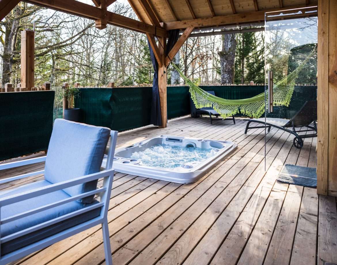 Hébergement insolite en cabane avec jacuzzi et hamac sur une terrasse en bois.