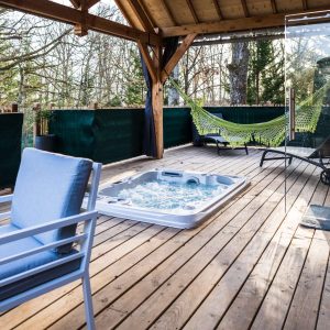 Hébergement insolite en cabane avec jacuzzi et hamac sur une terrasse en bois.