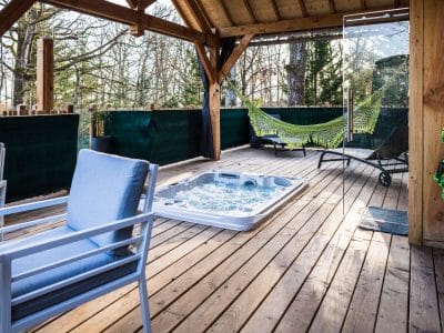 Hébergement insolite en cabane avec jacuzzi et hamac sur une terrasse en bois.