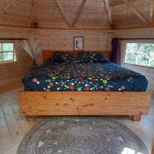 Cabane en bois avec lit coloré et tapis rond, au cœur de la nature en Midi-Pyrénées.