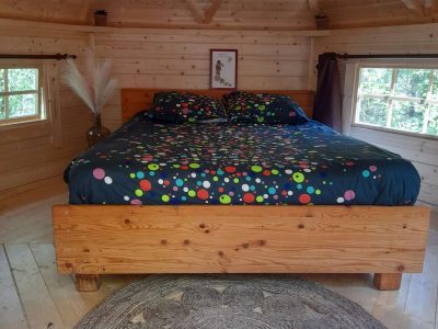 Cabane en bois avec lit coloré et tapis rond, au cœur de la nature en Midi-Pyrénées.
