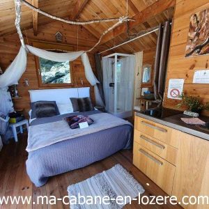 Cabane en bois cosy avec lit douillet et cuisine intégrée, au cœur de la nature.