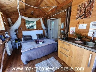 Cabane en bois cosy avec lit douillet et cuisine intégrée, au cœur de la nature.