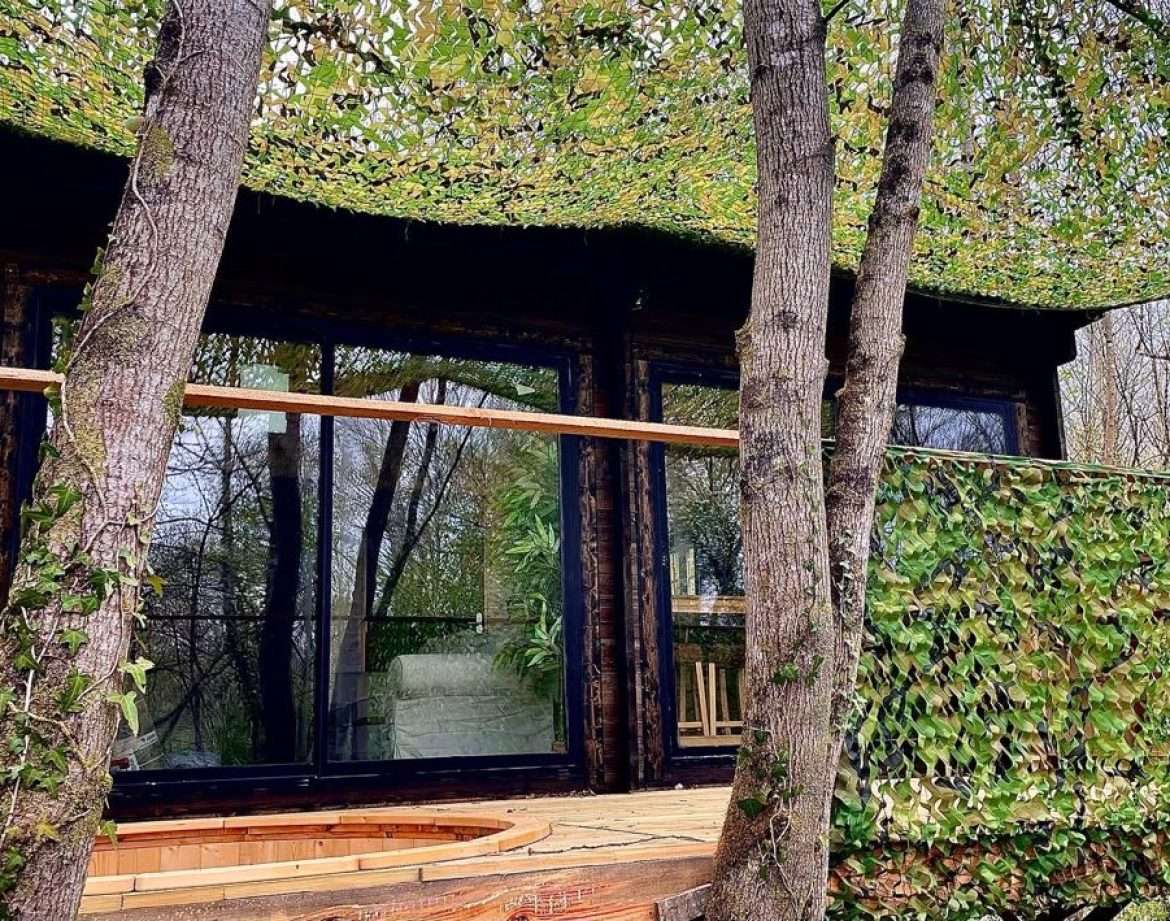 Cabane perchée camouflée dans les arbres, entourée de verdure à Midi-Pyrénées.