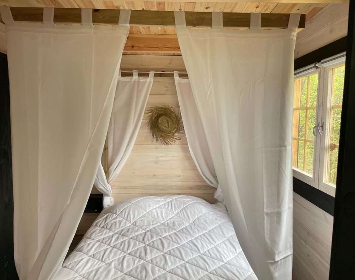 Cabane cosy en Midi-Pyrénées, lit douillet entouré de rideaux blancs.