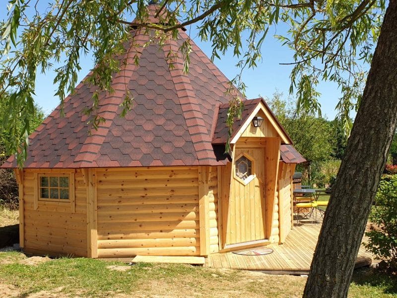 Cabane en bois ronde avec toit en ardoise, entourée de verdure paisible.