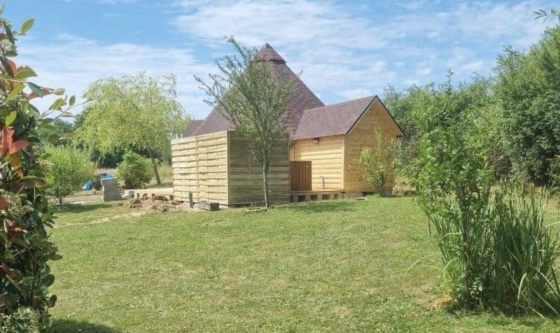 Charmante cabane en bois avec un toit pointu, entourée de verdure.