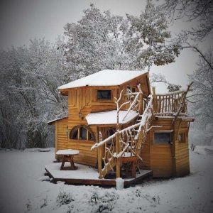 Cabane en bois perchée, entourée de neige et de nature paisible.