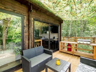 Cabane en bois avec terrasse, entourée de verdure, idéale pour un séjour nature.