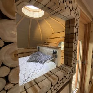 Cabane en bois avec un lit douillet et un miroir en rondins décoratif.