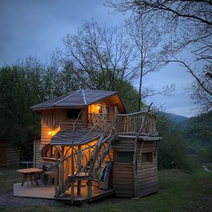 Cabane dans les arbres à Midi-Pyrénées, éclairée, entourée de verdure.