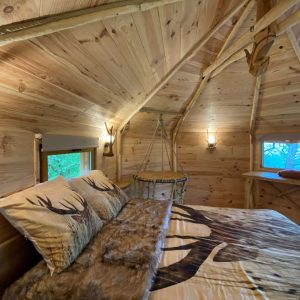 Cabane en bois avec lit douillet et décor naturel, ambiance chaleureuse.