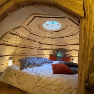 Cabane en bois avec un lit douillet, éclairage doux et fenêtre circulaire.