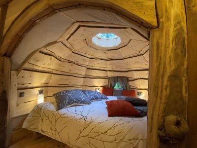 Cabane en bois avec un lit douillet, éclairage doux et fenêtre circulaire.