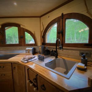 Cabane en bois avec fenêtres arrondies, offrant une vue sur la nature verdoyante.