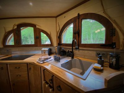 Cabane en bois avec fenêtres arrondies, offrant une vue sur la nature verdoyante.
