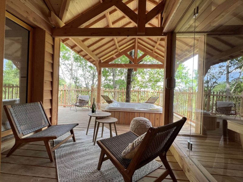 Cabane en bois avec jacuzzi, terrasse ensoleillée et fauteuils confortables.