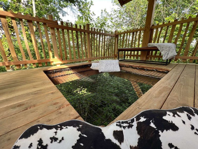 Cabane perchée avec terrasse en bois et vue sur la nature environnante.