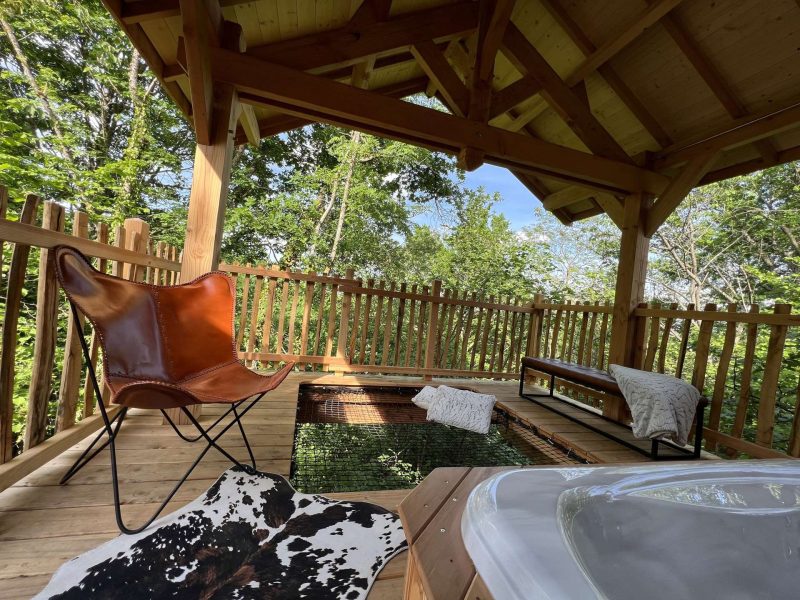 Hébergement insolite en Auvergne : cabane avec jacuzzi et fauteuil en cuir, entourée de verdure.
