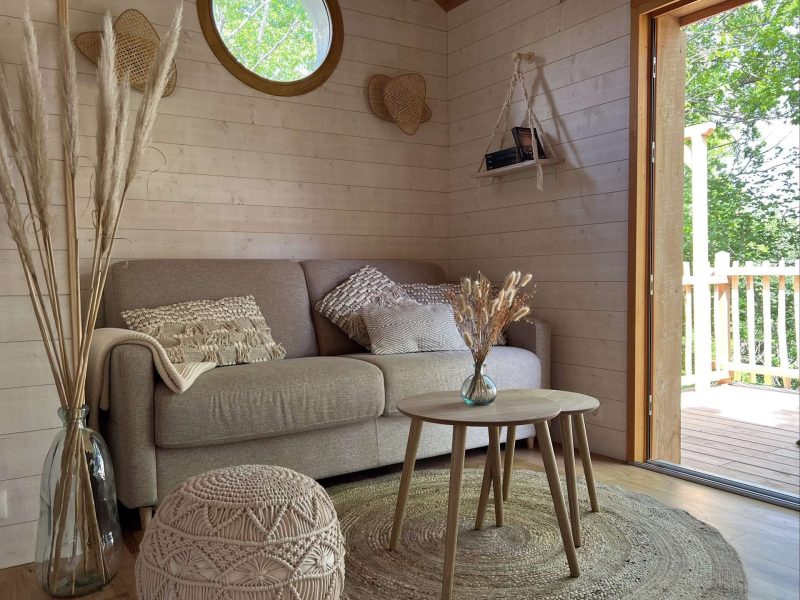 Cabane en bois avec un salon lumineux, canapé confortable et vue sur la nature.
