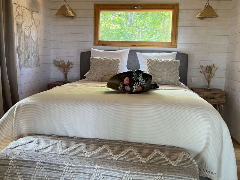 Chalet cosy avec lit douillet, décoré de fleurs et lumière naturelle.