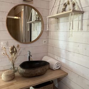 Hébergement insolite en Auvergne : salle de bain moderne avec lavabo en pierre et miroir rond.