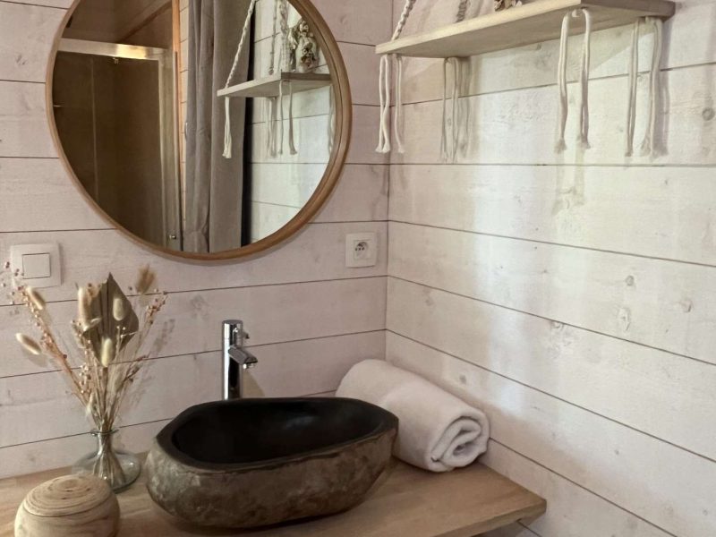 Salle de bain moderne dans un chalet en bois, avec un lavabo en pierre et un miroir rond.