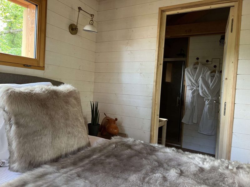 Chalet cosy avec lit douillet, décoré de fourrures et accès à une salle de bain moderne.