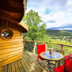 Cabane perchée avec vue panoramique, terrasse en bois et table colorée.
