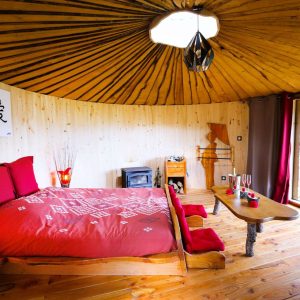 Hébergement insolite en yourte, intérieur en bois chaleureux avec lit douillet et vue.