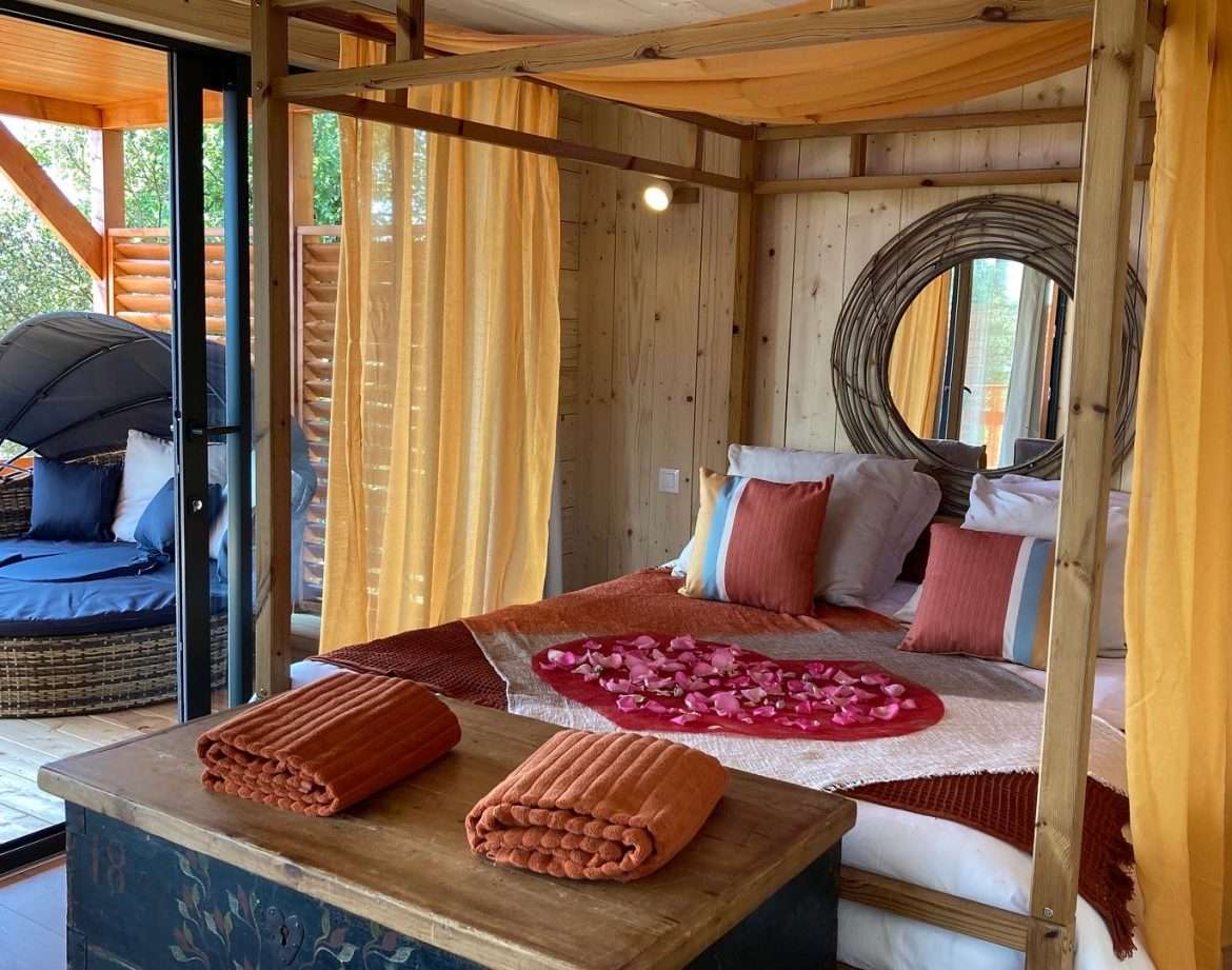 Chambre romantique en cabane, décorée de pétales de rose et drapée de voiles.
