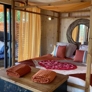 Chambre romantique en cabane, décorée de pétales de rose et drapée de voiles.