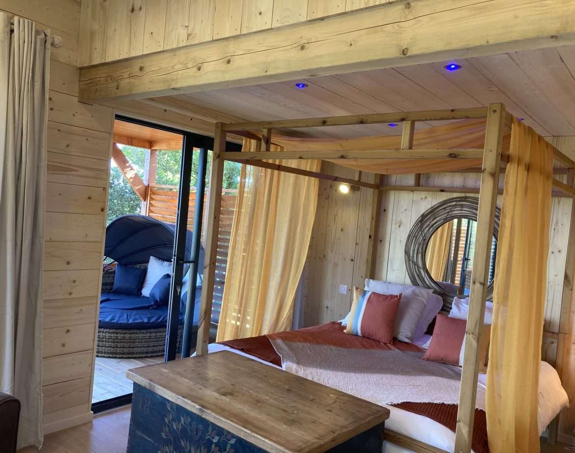 Hébergement insolite en bois avec lit à baldaquin et coin détente extérieur.