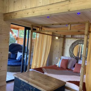 Hébergement insolite en bois avec lit à baldaquin et coin détente extérieur.