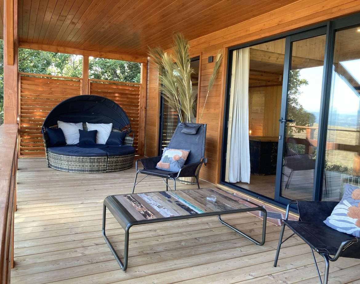Hébergement insolite en bois avec terrasse, fauteuils confortables et vue dégagée.