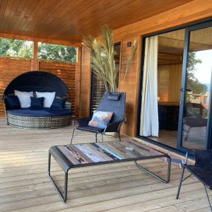 Hébergement insolite en bois avec terrasse, fauteuils confortables et vue dégagée.