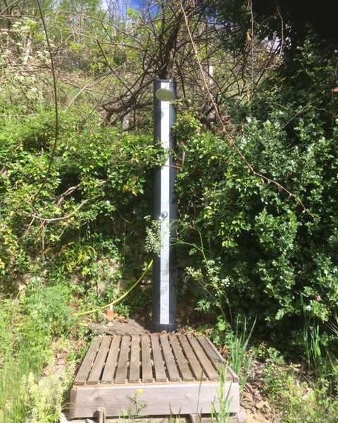 Douche extérieure en bois, entourée de verdure, idéale pour un camping nature.