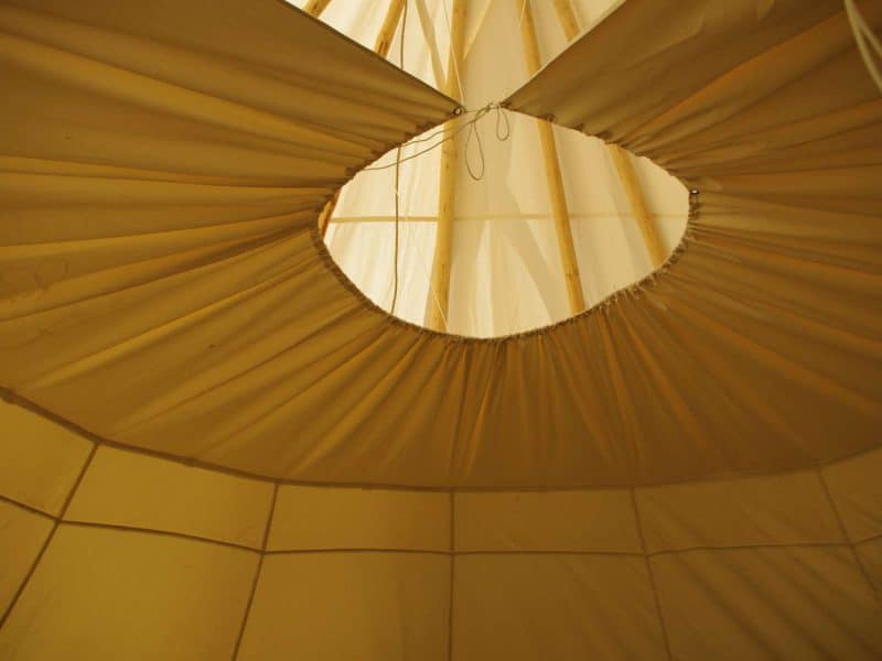 Intérieur dun tipi avec un plafond en toile beige et une ouverture circulaire.