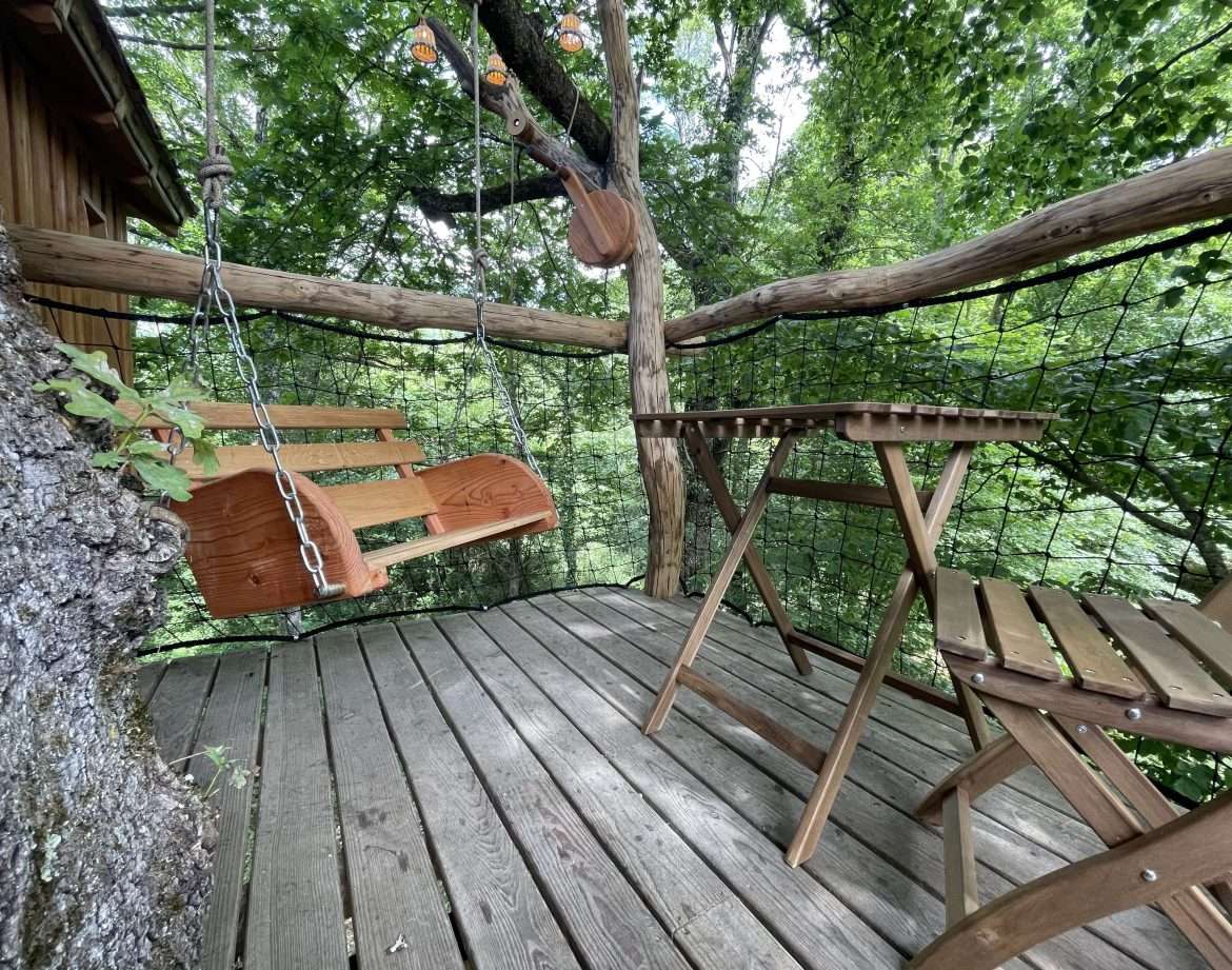Cabane perchée en Aquitaine avec balancelle en bois et vue sur la nature environnante.