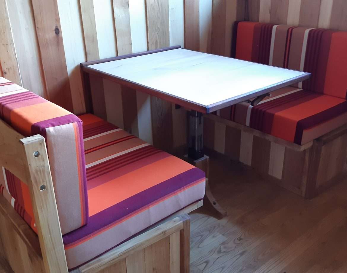 Hébergement insolite en Aquitaine : coin repas en bois avec banquettes colorées.