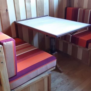 Hébergement insolite en Aquitaine : coin repas en bois avec banquettes colorées.